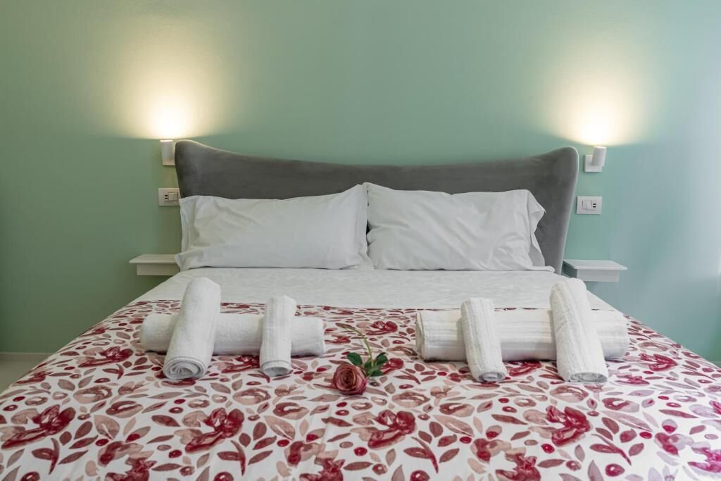 A neatly made bed with white linens, a floral-patterned bedspread, and rolled towels on the bed.