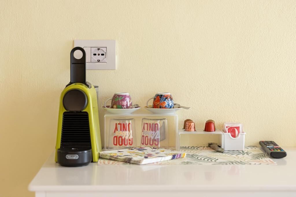 A small table with a vacuum cleaner, a magazine, a remote control, and a small shelf with mugs and a decorative item.
