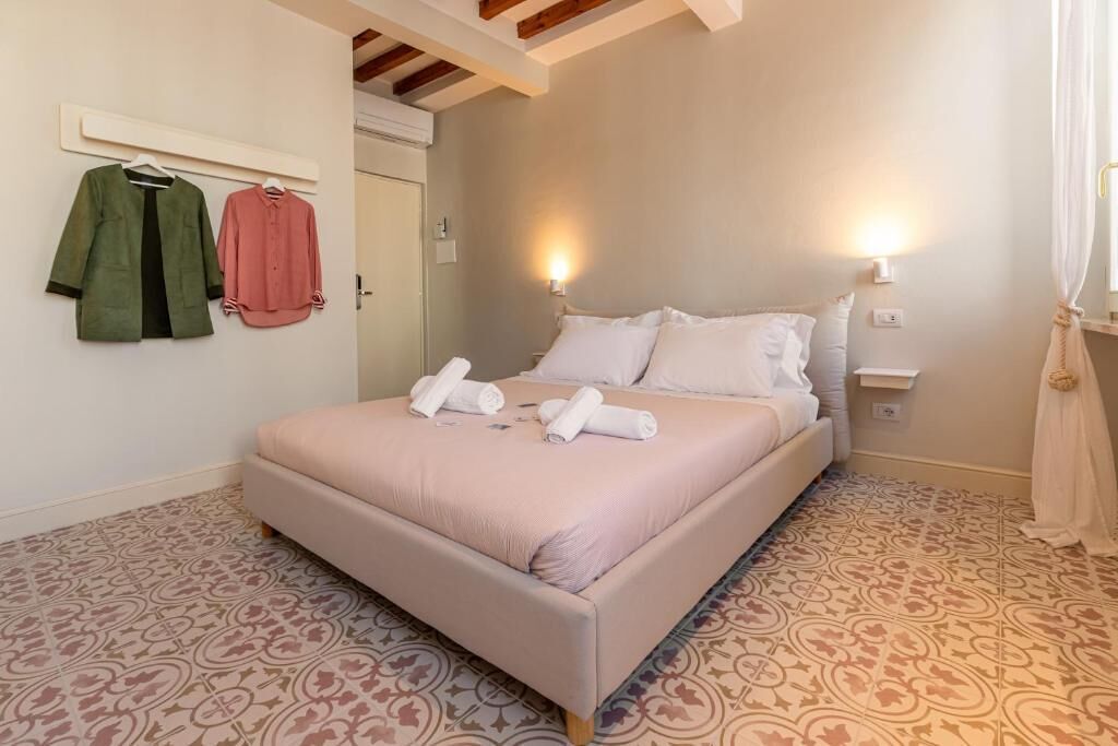 A bedroom with a bed, two wall-mounted lamps, a door, and patterned floor tiles.