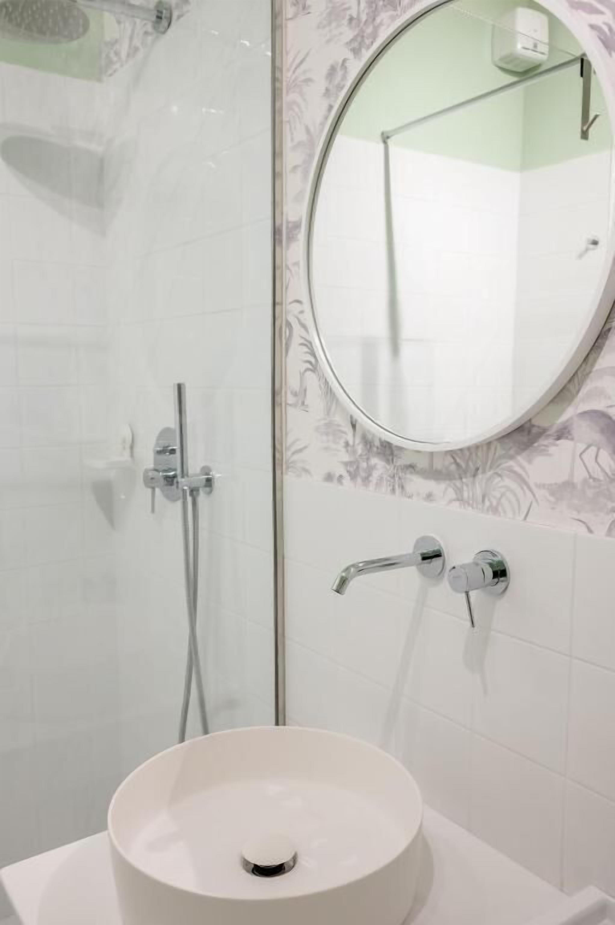 Un bany amb una cabina de dutxa de vidre, un mirall rodó i un lavabo blanc.