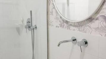 Un bany amb una cabina de dutxa de vidre, un mirall rodó i un lavabo blanc.