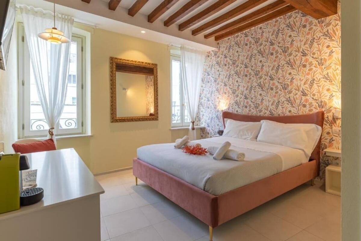 A bedroom with a bed, a bedside table, a mirror, and a window with curtains.