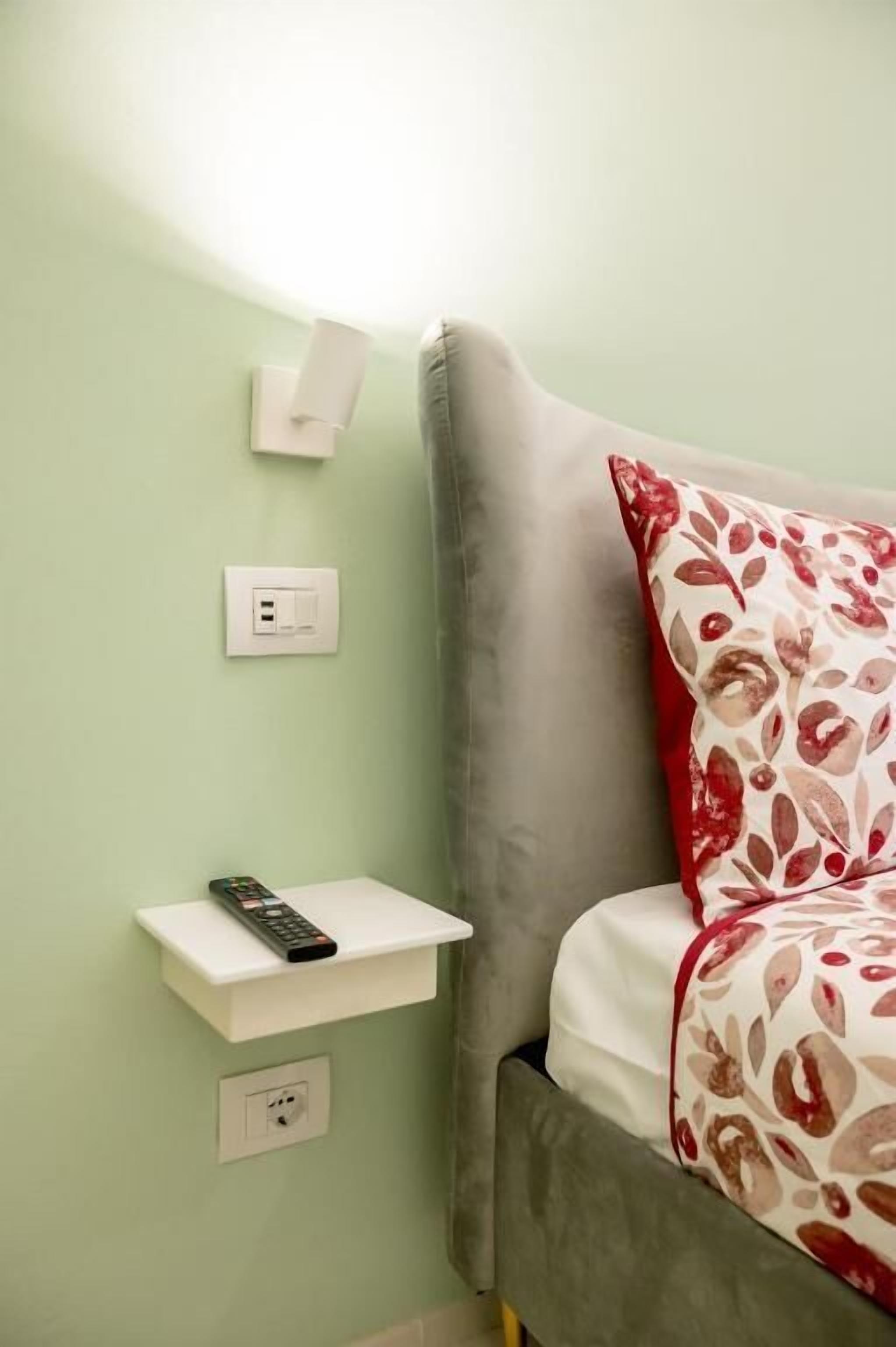 Un lit avec un oreiller à motifs floraux, une table de chevet avec une télécommande et deux prises électriques murales.