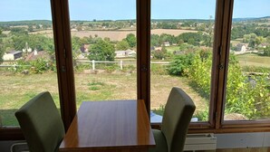 A room with a table and chairs, large windows with a view of a rural landscape. - Charming gîte with panoramic views over the hills of the Morvan (James)