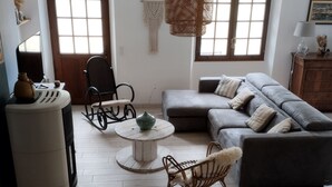 Een woonkamer met een bank, stoelen, een tafel en een decoratieve hanglamp.