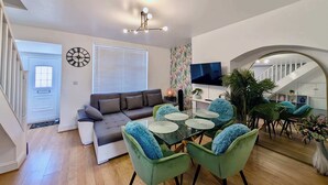 En moderne stue med sofa, spisebord, stole, fjernsyn og trappe.