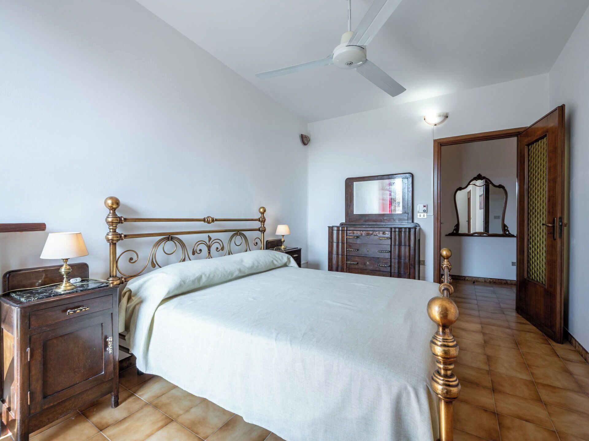 A bedroom with a bed, nightstands, a dresser, a ceiling fan, and a mirror.