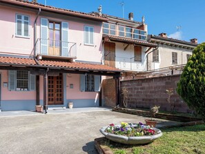 Un edificio de dos pisos con un balcón, un parterre floral en primer plano y una pared de ladrillo.