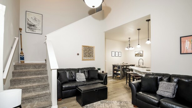 Uma sala de estar moderna com escada, um sofá de couro preto, área de jantar e cozinha.
