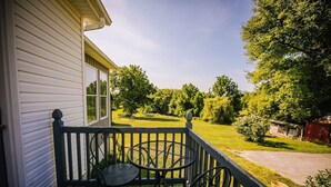 Eine Veranda mit Tisch und Stühlen, ein Haus mit weißem Putz und ein grüner Rasen mit Bäumen.