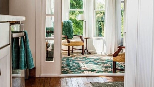 Ein Zimmer mit Holzboden, Deckenventilator, Ausblick ins Freie und einem Stuhl am Fenster.