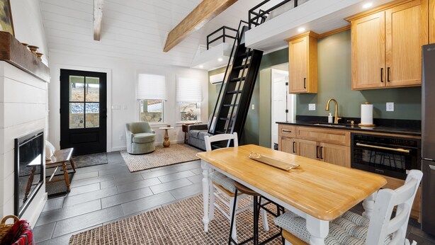 A modern kitchen with a wooden table, white chairs, a black ladder, and wooden cabinets.