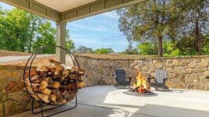 An outdoor patio with a stone wall, a fire pit, and two Adirondack chairs.