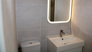Un baño con inodoro, lavamanos y espejo con luz.