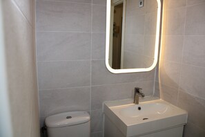 Ein Badezimmer mit Toilette, Waschbecken und einem beleuchteten Spiegel.