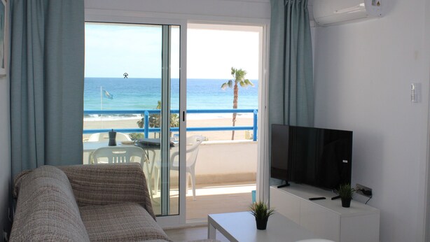 Una habitación con sofá, televisor, una mesita y balcón con vistas a la playa y al océano.