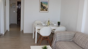 Un comedor con una mesa dispuesta para dos, un sofá y una planta en maceta sobre una mesa blanca.