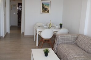 Ein Essbereich mit einem für zwei Personen gedecktem Tisch, einer Couch und einem Blumentopf auf einem weißen Tisch.
