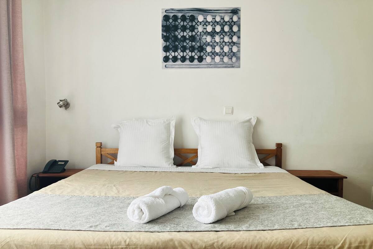 A neatly made bed with two pillows, a bedside table with a phone, and a wall-mounted chessboard.
