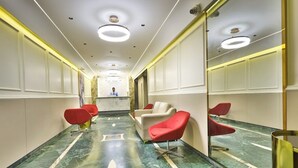 A hotel lobby with a reception desk, red and white chairs, marble flooring, and a mirrored wall.