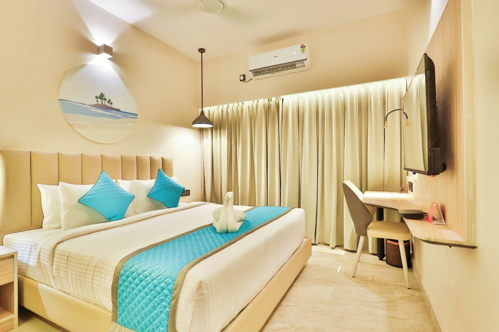Habitación de hotel con cama, escritorio, silla, televisor, aire acondicionado y una obra de arte colgada en la pared.