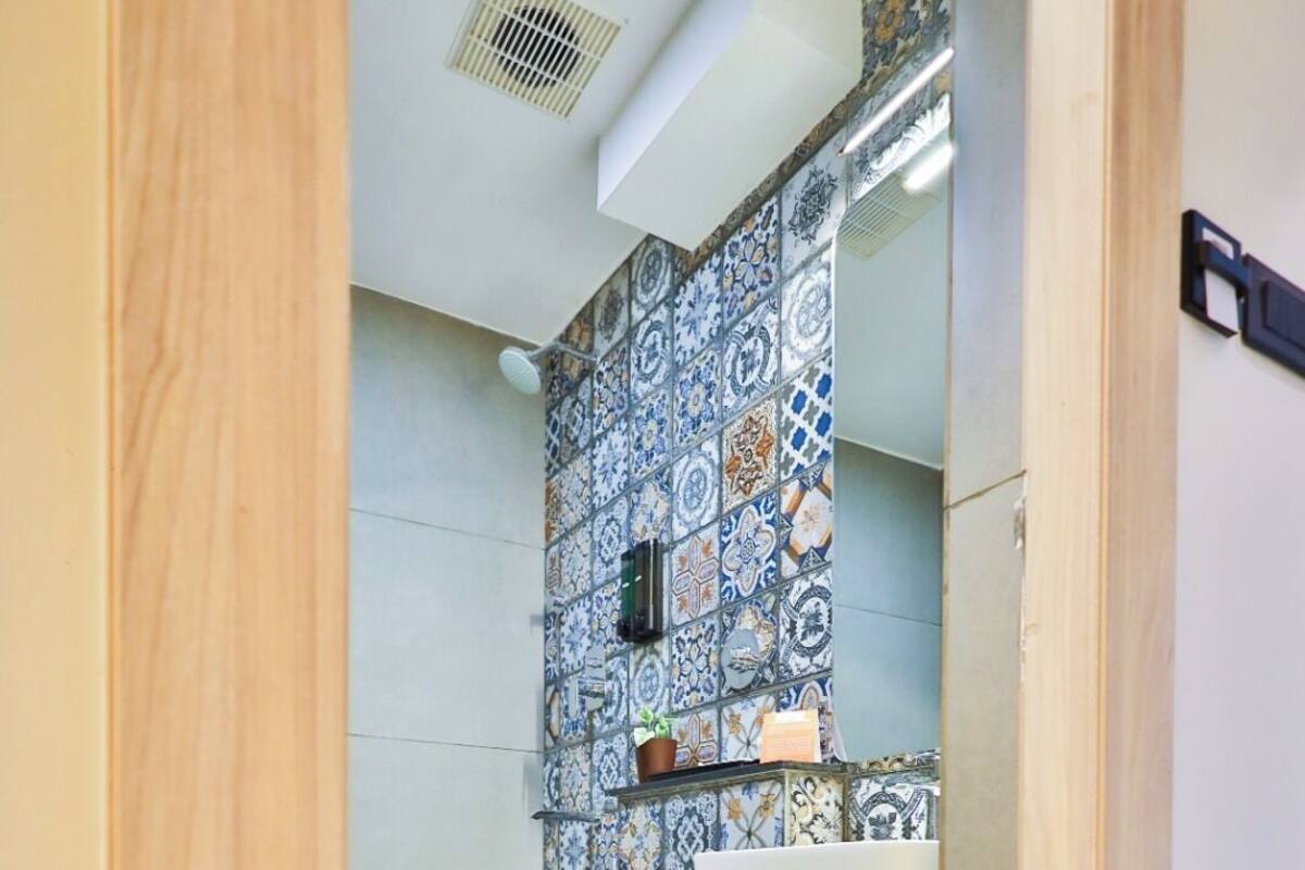 Une salle de bain avec des toilettes, un lavabo avec une étagère rose et un mur carrelé orné d’un motif décoratif.