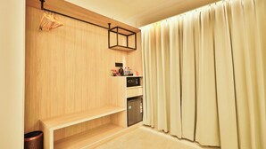 A room with a wooden bench, a hanging coat rack, a microwave, and a small shelf with items.