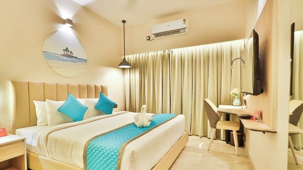 A hotel room with a bed, a desk, a chair, a TV, and an air conditioning unit.