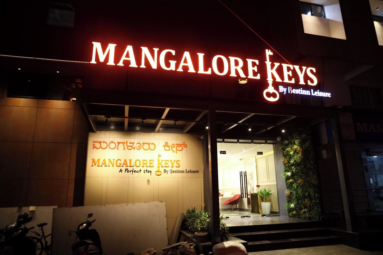 A hotel entrance with signage for 'Mangalore Keys' and a sign in a local language.