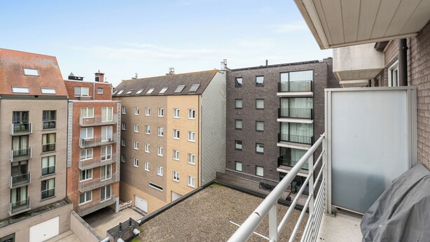 Un edificio residenziale a più piani con balconi, un cortile in ghiaia e cielo sereno.