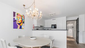 Una cucina moderna con mobili bianchi, un tavolo da pranzo con sedie, un lampadario e un quadro colorato appeso al muro.