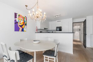 A modern kitchen with white cabinetry, a dining table with chairs, a chandelier, and a colorful painting on the wall. - Dukdalf 20 0403 + G-2/17 (Nieuwpoort)