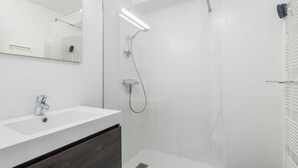 Un bagno moderno con un lavandino bianco, uno specchio, una doccia con soffione a mano e un porta asciugamani.