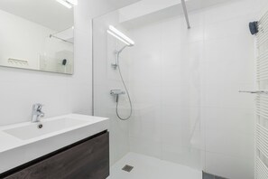 A modern bathroom with a white sink, a mirror, a shower with a handheld showerhead, and a towel rack. - Dukdalf 20 0403 + G-2/17 (Nieuwpoort)