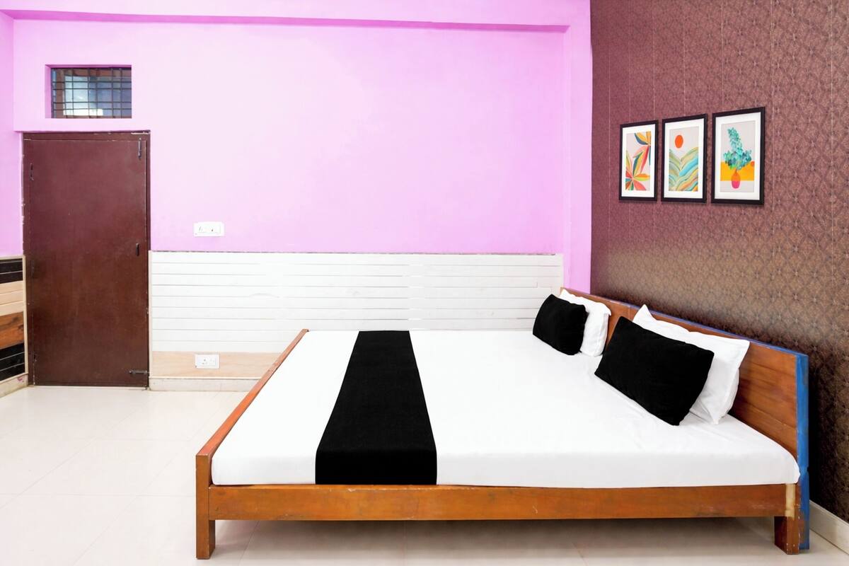 A bedroom with a wooden bed, white bedding, a black runner, a brown door, and a pink wall with three framed pictures.
