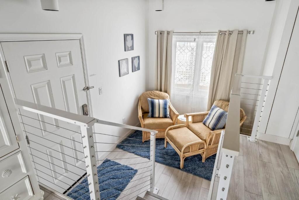 A staircase leading to a room with a sofa, two chairs, a window with curtains, and a door.