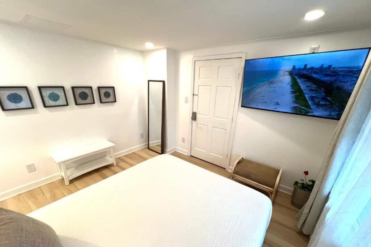 A bedroom with a bed, a TV, a door, and a small bench.