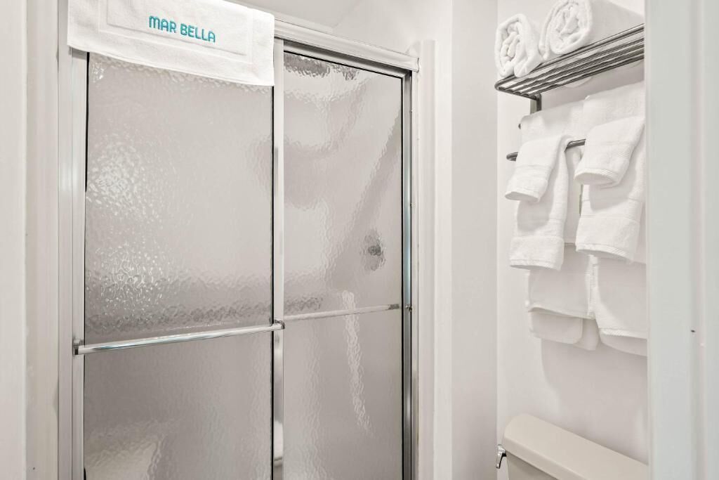 A bathroom with a frosted glass shower door, a towel rack with folded towels, and a toilet visible.
