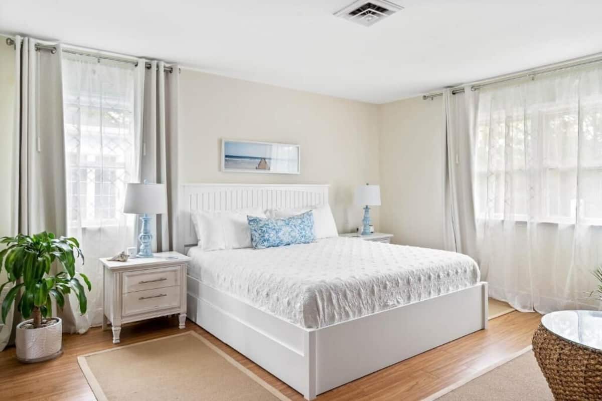 A bedroom with a bed, nightstands, a potted plant, and a window with curtains.