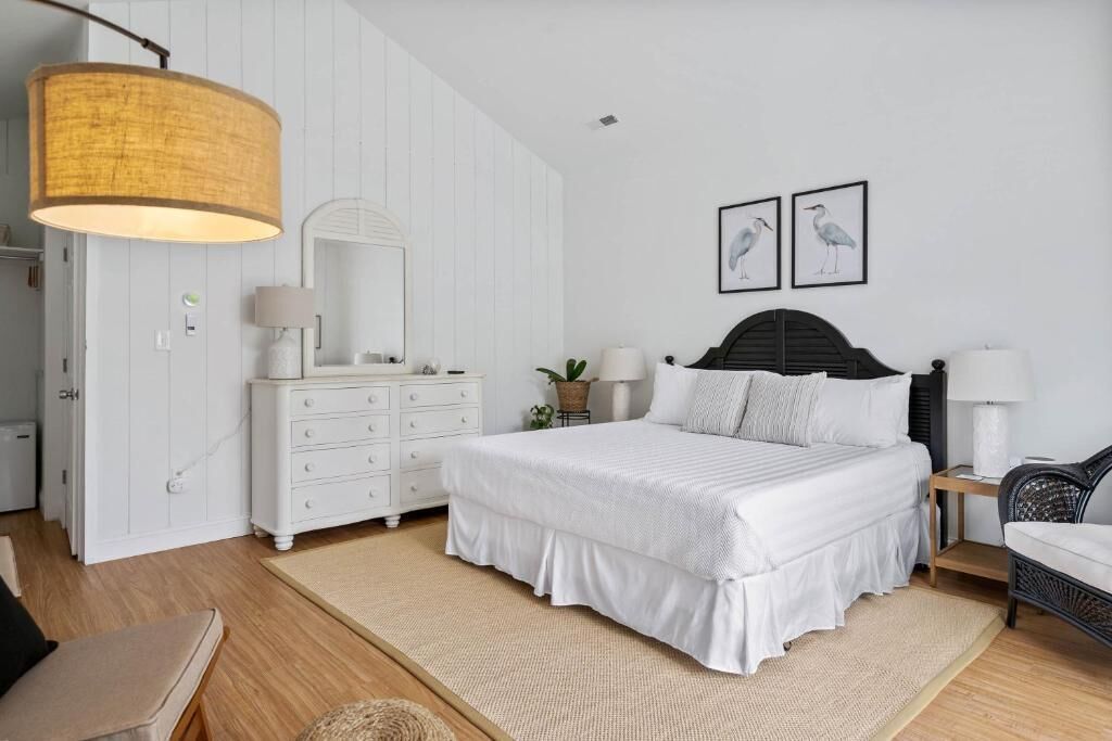 A bedroom with a bed, white dresser, bedside tables, a large hanging lamp, and wall art.