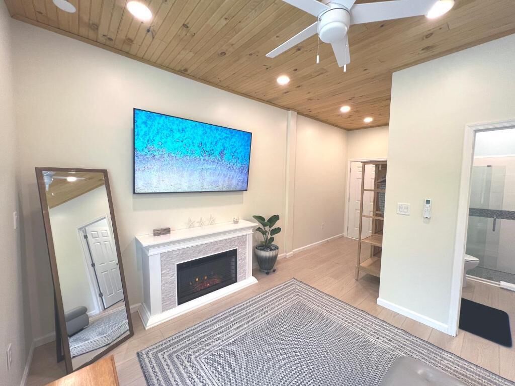 A living room with a fireplace, a large flat-screen TV, a ceiling fan, and a mirrored wall.