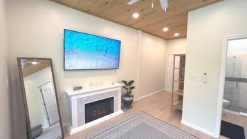 A living room with a fireplace, a large flat-screen TV, a ceiling fan, and a mirrored wall.