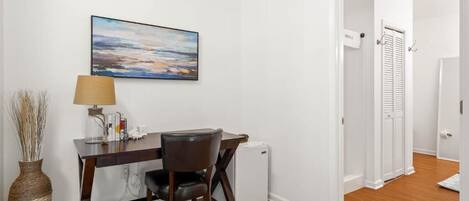 Una stanza con una scrivania, una sedia, una lampada e un quadro appeso al muro.