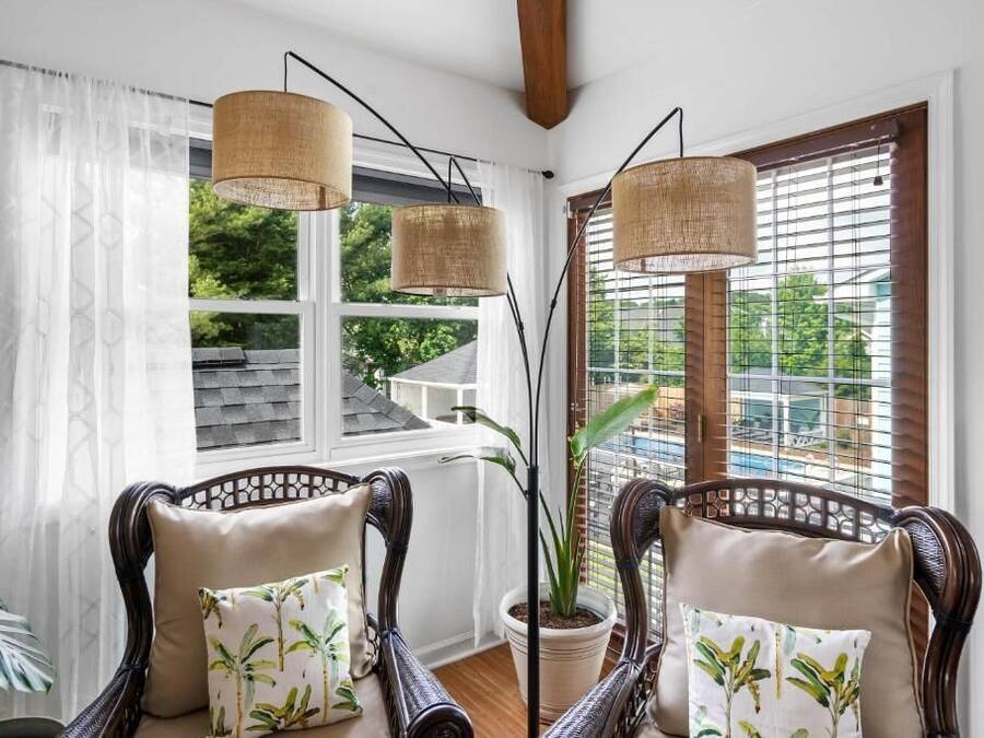 A room with wicker chairs, a potted plant, and a view through a window with blinds.