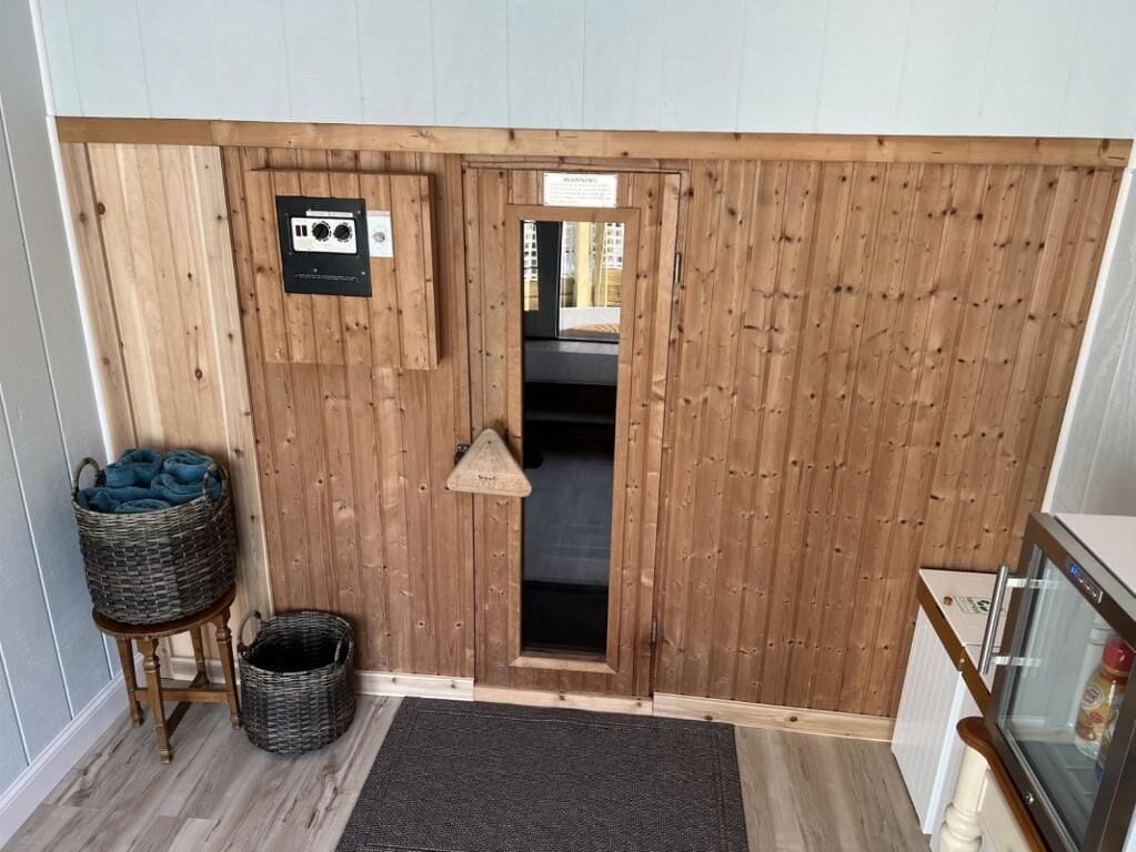 A room with a wooden door, a small basket, a mat, and a refrigerator.