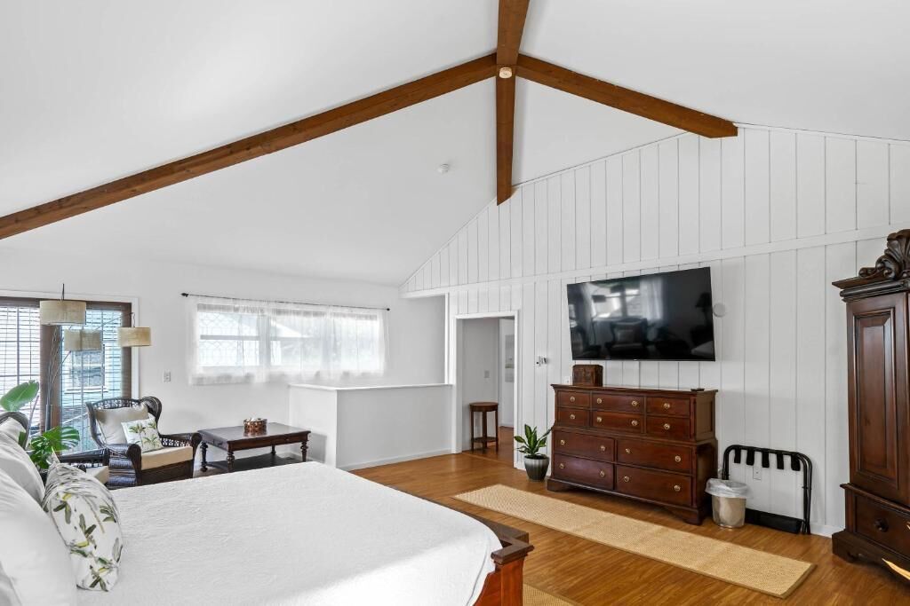 A spacious bedroom with a large bed, wooden ceiling beams, a television, and a dresser.