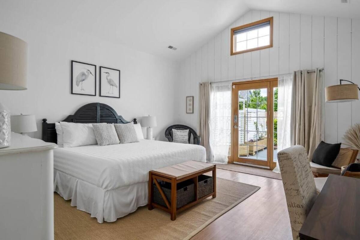 A bedroom with a bed, bedside tables, a chair, a window, and a door leading to a balcony.