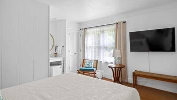 Habitación de hotel con cama, televisión, silla, mesita y ventana con cortinas.