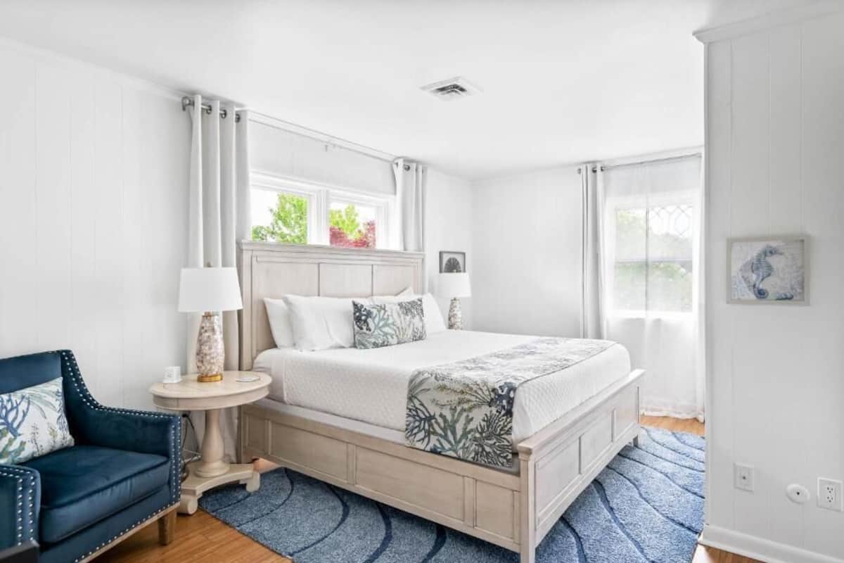 A bedroom with a bed, a chair, a bedside table, and a window.