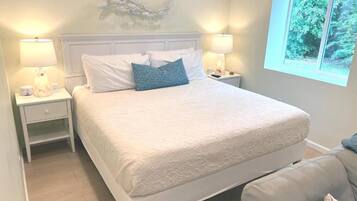 A bedroom with a large bed, two bedside tables with lamps, a decorative wall piece, and a window with a view of greenery.